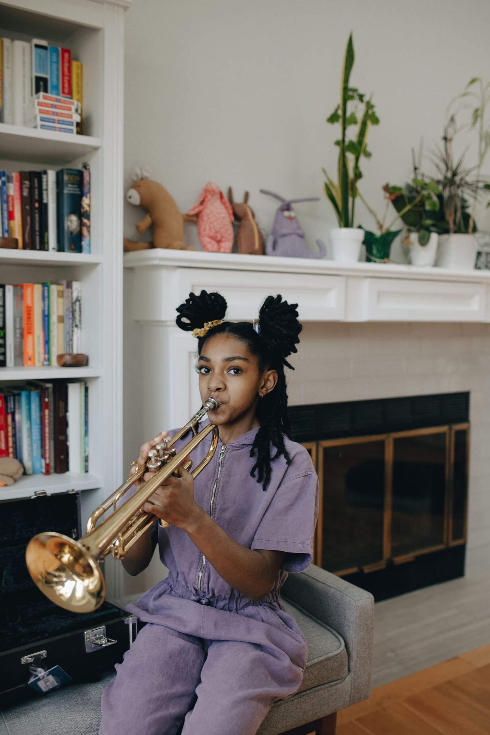 A young girl is playing a brass trumpet while sitting indoors