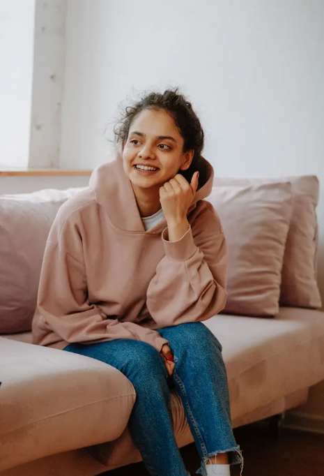 A smiling young woman with dark curly hair sitting on a beige couch