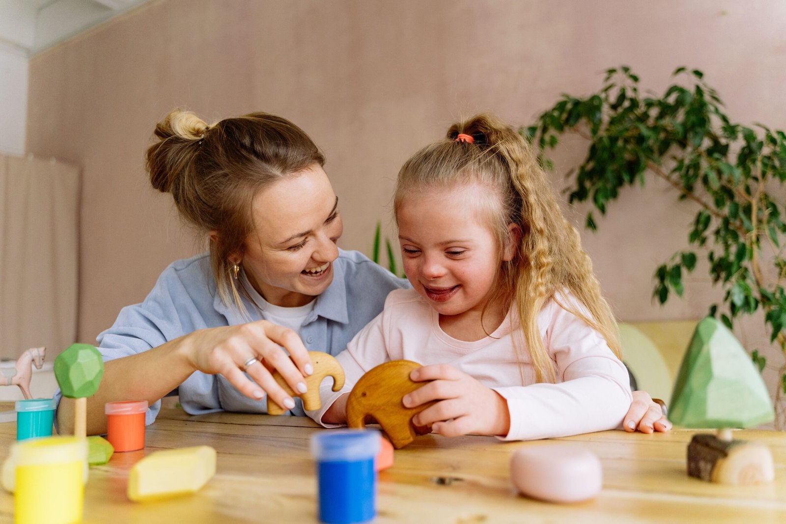 A woman and a young child smiling while sitting together at a wooden table and playing