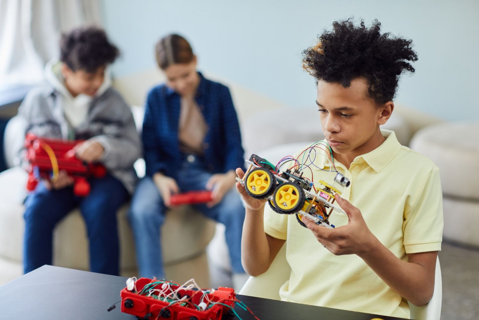 A young boy in a yellow polo shirt holding and assembling a small robotic car