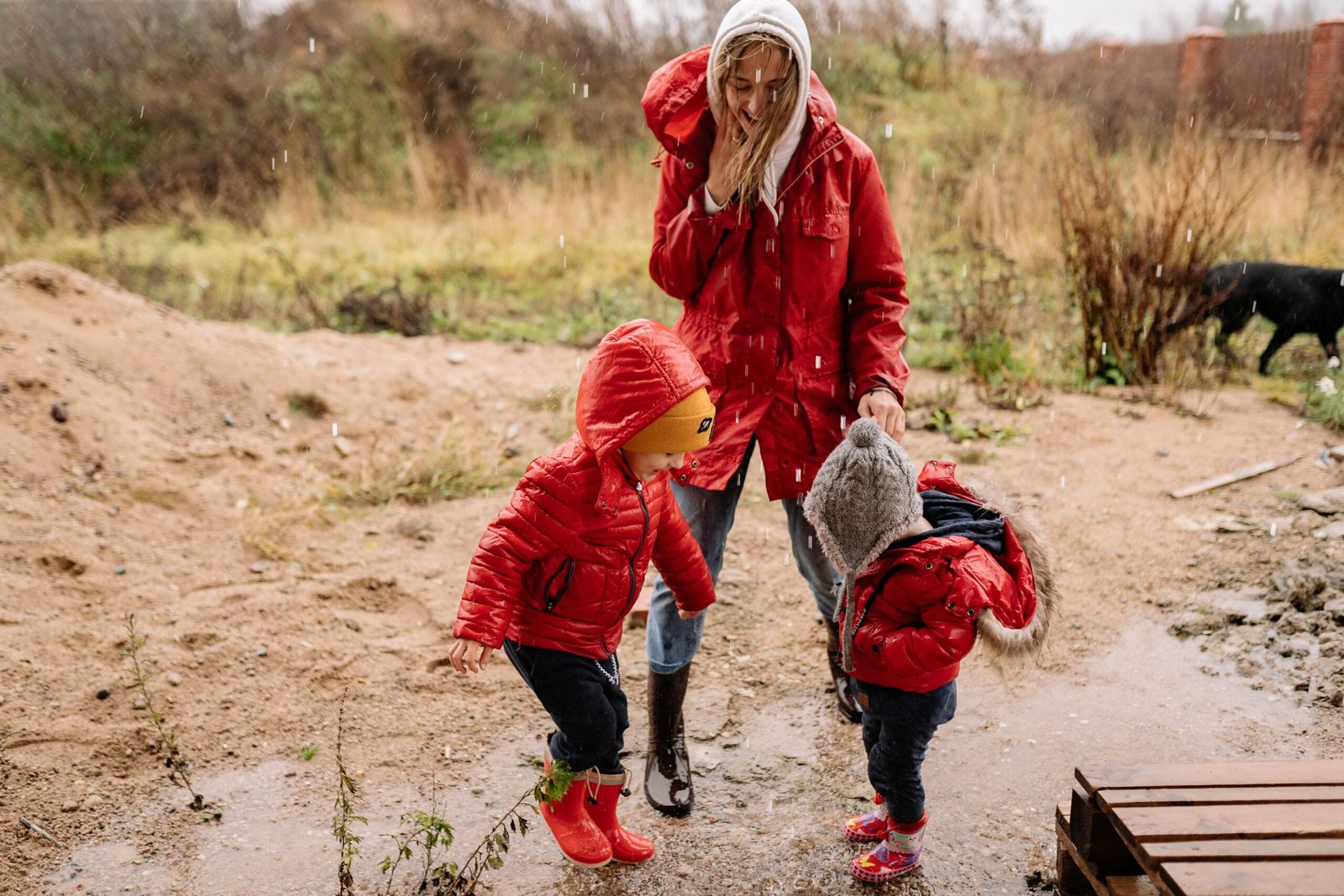 A mother and two young children playing and splashing in a puddle
